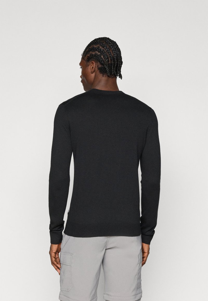 Pullover nero a maniche lunghe con texture a coste e collo tondo, mostrato di spalle. Indossato con pantaloni corti grigi chiari.