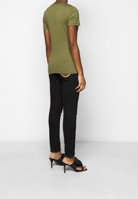 Olivově zelené přiléhavé tričko s krátkým rukávem, spárované s černými skinny jeans. Černé sandály na vysokém podpatku s dekorační mašlí.
