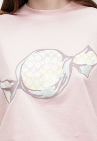 Ροζ βαμβακερό μπλουζάκι με μεγάλο, στιλιζαρισμένο σχέδιο γλυφιτζούρι σε ασημί και παστέλ αποχρώσεις, με διακριτικές λεπτομέρειες περιτυλίγματος.