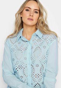 Camicia azzurro chiaro con bottoni, caratterizzata da un design floreale ritagliato, con colletto e maniche lunghe, realizzata in un tessuto leggero.