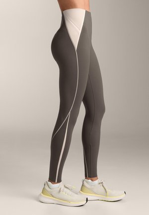 Legice s sivimi in bež ukrivljenimi paneli, nošene z belimi in rumenimi športnimi copati na nevtralnem ozadju.