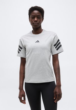 Γυναίκα που φοράει γκρι μπλούζα Adidas με μαύρο λογότυπο στο στήθος και τρεις μαύρες ρίγες σε κάθε μανίκι, συνδυασμένη με μαύρο κολάν.