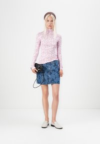 Maglietta rosa a maniche lunghe con stampa floreale, gonna di jeans con motivo testurizzato, scarpe bianche slip-on e una piccola borsa nera.