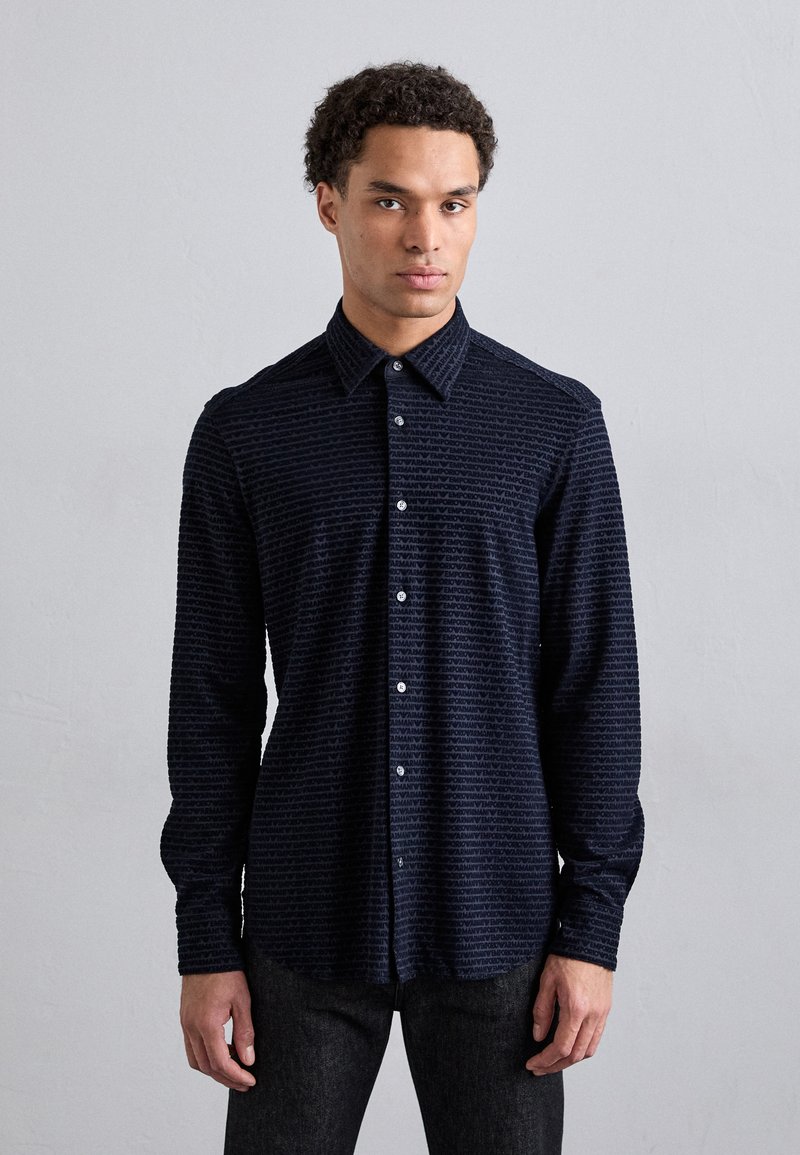Maglietta a maniche lunghe blu navy con un motivo testurizzato, colletto con bottoni e bottoni frontali, realizzata in un tessuto morbido con una leggera lucentezza.
