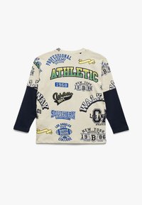 Beige Langarm-T-Shirt aus Baumwolle mit blauen und marineblauen Ärmeln. Verfügt über verschiedene sportliche Druckmotive in verschiedenen Farben und Größen.