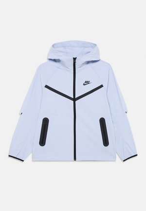 Helleblaue Nike-Jacke mit Kapuze, mit einem schwarzen Reißverschluss an der Vorderseite, schwarzen Akzenten und zwei seitlichen Reißverschlusstaschen. Glatte Stoffstruktur.