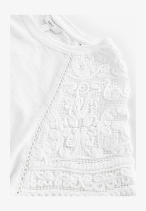 Witte t-shirt met ingewikkelde, textuurvolle borduurwerk aan de ene kant en een gladde afwerking aan de andere kant. Ronde halslijn met delicate details.