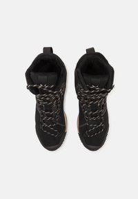 Botas negras de caña alta con parte superior de material sintético, tela texturizada, cordones gruesos en gris y una lengüeta en la parte posterior. Suela de goma ligera.