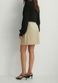 Pull noir côtelé avec des manches longues associé à une mini-jupe en satin beige et des sandales à talons noires à lanières. Texture de tissu lisse.