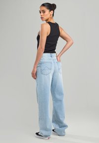 Black sleeveless top paired with light blue oversized denim jeans. Jeans feature five pockets and a subtle triangular design on the rear pockets.