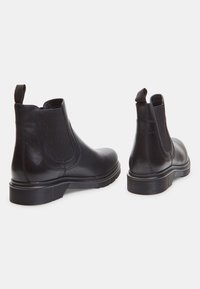 Des bottes Chelsea en cuir noir dotées de panneaux élastiques sur les côtés, d'une languette et d'une semelle texturée. Le design est épuré avec des finitions lisses.