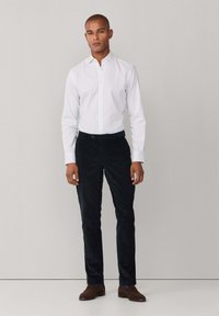 Witte button-up shirt met een subtiele ruitjespatroon, gecombineerd met marineblauwe corduroy broeken en bruine schoenen, met een getailleerde pasvorm.