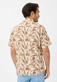 Camicia a maniche corte con bottoni di colore beige decorata con un motivo floreale nei toni del marrone e del blu. Presenta un colletto e una vestibilità comoda.