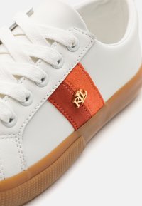 Baskets en cuir blanc avec lacets blancs, semelle en gomme, et un patch en daim rouge avec un logo doré "RLL" sur le côté.