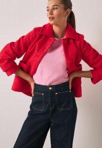 Rød uldblandet jakke med lommer, lyserød sweater og mørkeblå højttaljede jeans i denim. Outfit'et har et tekstureret, hyggeligt udseende.