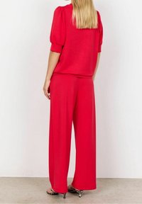 Top rojo de gran tamaño con mangas abullonadas, combinado con pantalones de pierna ancha, ambos en una tela suave, usados con sandalias de tacón con estampado de animal.