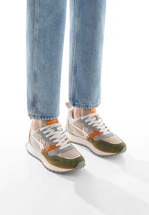 Sneaker beige e verde oliva con accenti bianchi, tomaia in suede texturizzato e rete, con dettagli arancioni e lacci bianchi su una suola chunky.