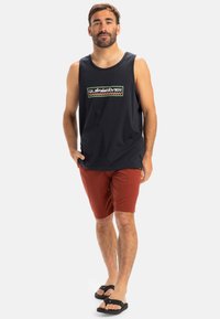 Navy tank top with a graphic logo, paired with rust-colored shorts. Sandals in black. Simple design, cotton material, no patterns.