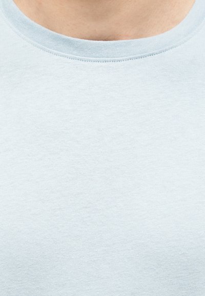 Κοντινό πλάνο ανοιχτό μπλε T-shirt με στρογγυλή λαιμόκοψη, που φοριέται στην ανώτερη περιοχή του στήθους και του λαιμού ενός ατόμου.