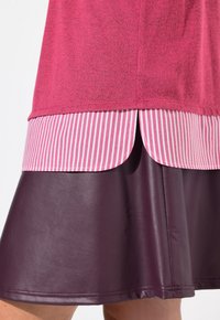 Rosa topp lager på en randig rosa och vit blus, parat med en mörk lila fuskläderkjol. Synlig sömnad och fålldetaljer.