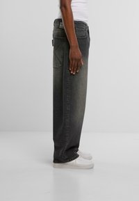 Vaqueros negros holgados y descoloridos con cintura alta, que cuentan con un bolsillo trasero y una etiqueta de marca en la cinturilla, combinados con zapatillas blancas.