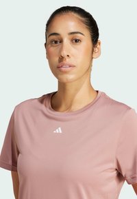 Ljust rosa tränings T-shirt med korta ärmar, med en vit logotyp på bröstet. Slät textur och rundad halsringning.