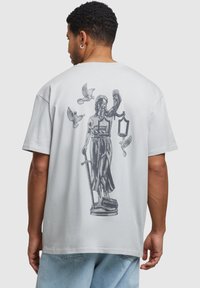 Light gray cotton t-shirt featuring a detailed graphic of a statue holding scales and a lantern, surrounded by flying birds on the back.