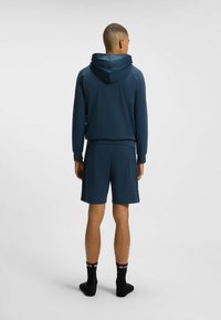 Felpa atletica blu navy con pantaloni corti abbinati. Tessuto morbido con una vestibilità comoda, dotata di cappuccio con coulisse e polsini a coste. Calzini neri.