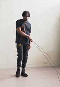 Sort T-shirt med orange grafik, parret med sorte sweatpants med "UFC" i gul. Sorte høj-top sneakers med røde såler.
