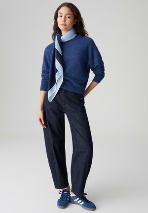 Blue wool sweater with a high neckline, paired with dark denim wide-leg pants and blue sneakers featuring white stripes. Light blue scarf accent.