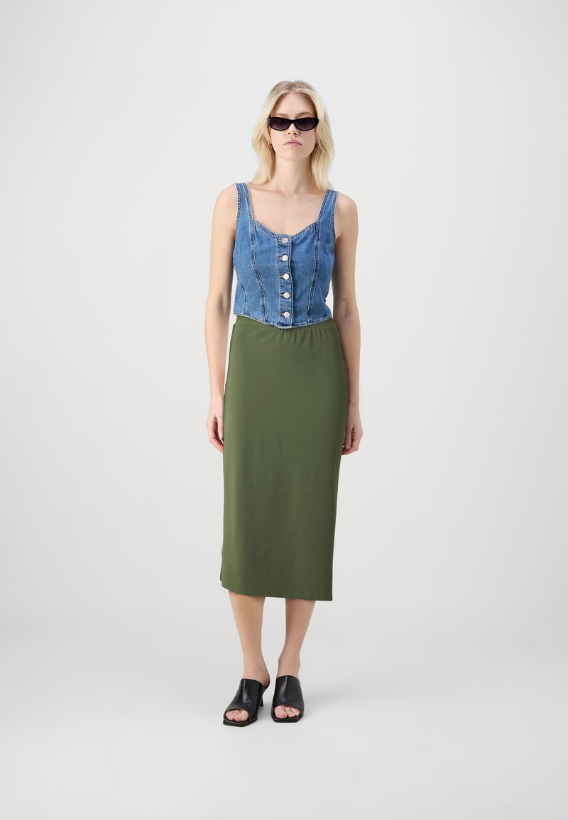 Jeans crop topp med knappelukking, kombinert med en ensfarget olivengrønn midiskjørt. Svart åpen-tå sko. Jevn stofftekstur.