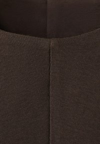 Zbliżenie na ciemnobrązową prążkowaną tkaninę z centralnym szwem tworzącym kształt litery V, ukazujące fakturę i szczegóły szwów.