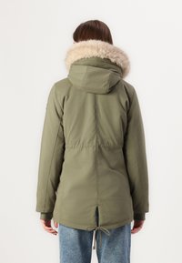 Olive rohelise pargaga, millel on vale karva voodriga kapuuts, reguleeritav tõmblukuga vöökoht ja küljetaskud. Omab pikki varrukaid ja sujuvat tekstuuri.