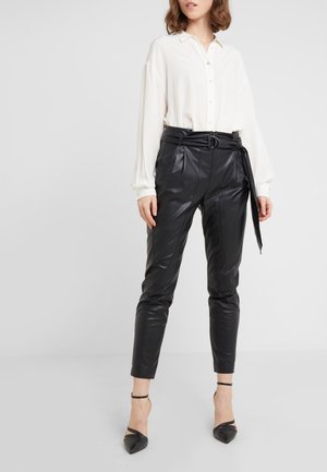 Chemise blanche à manches longues, assortie à un pantalon en simili cuir noir avec une taille haute ceinturée et une coupe ajustée. Escarpins noirs à talons aiguilles.