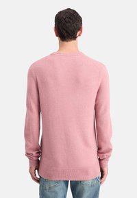 Suéter rosa claro con una textura suave, mangas largas, diseño de cuello redondo, puños y dobladillo de canalé, combinado con jeans azules.