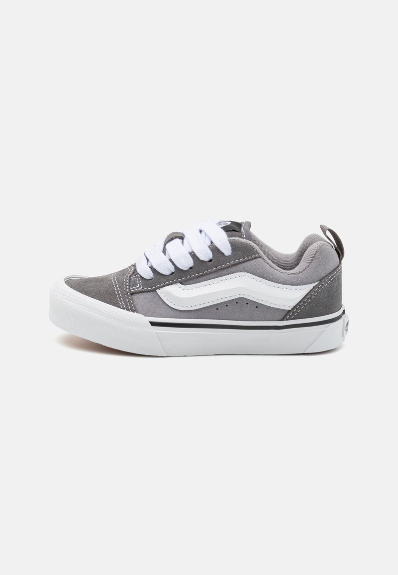 Baskets en daim gris avec des accents blancs, bout rond, lacets blancs et une bande noire le long de la semelle ; possède une languette au talon.