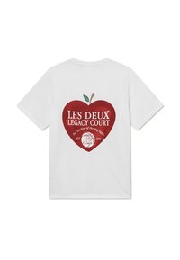 Bílá krátká tričko s grafickým zobrazením červeného jablka se zeleným listem. Text zní "LES DEUX LEGACY COURT" a "Pro lásku k Velkému Jablku."