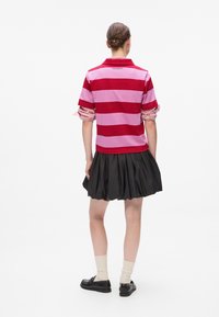 Polo rose et rouge à rayures avec des poignets à carreaux retroussés, associé à une jupe plissée noire et des chaussures noires à lacets.