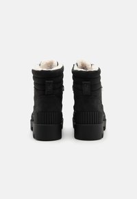 Bottines noires en daim avec un dessus rembourré, doublure en fausse fourrure, semelle en caoutchouc nervuré et une languette à l'arrière. Aucun détail de matériel visible.