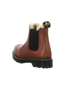 Botín de cuero marrón con paneles laterales elásticos negros, forro de piel sintética, costuras amarillas y una lengüeta en la parte trasera. Suela de goma.