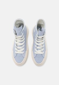 Pár světle modrých vysokých plátěných tenisek s bílými tkaničkami a krémovými gumovými podrážkami, viděný z výšky na bílém pozadí.