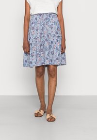 Blue floral skirt with tiered design, featuring pink and white patterns. Paired with tan slip-on sandals adorned with a gold buckle.