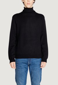 Maglione a collo alto nero con un design a maglia strutturata, caratterizzato da maniche lunghe e polsini a costine, abbinato a jeans blu.