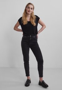 Sorte, tettsittende jeans med høy midje, kombinert med en løs svart t-skjorte. Antrekket har et minimalistisk design og stilige svarte sko.