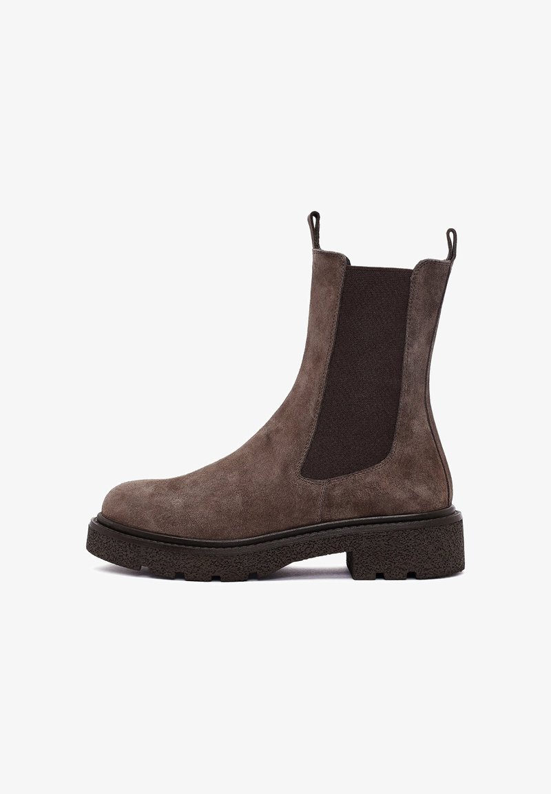 Bota chelsea de ante marrón con paneles laterales elásticos oscuros, pestañas para tirar y una suela de goma negra texturizada. Acabado suave con puntera redondeada.