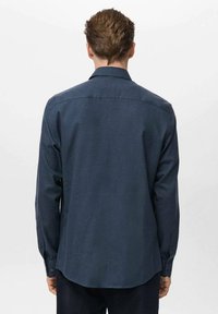Camisa de manga larga azul oscura con cuello abotonado, hecha de un tejido texturizado, con botones en los puños y un dobladillo curvado.