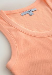 Débardeur côtelé couleur pêche douce avec un col rond et un design sans manches, avec une étiquette de marque blanche "NEXT" à l'intérieur du col.