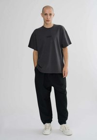 Dark gray oversized t-shirt with a subtle logo, paired with loose black trousers and white sneakers, creating a monochrome casual look.