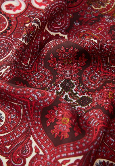 Red and cream paisley patterned fabric with intricate floral designs, smooth texture, and a rich, dark brown background.