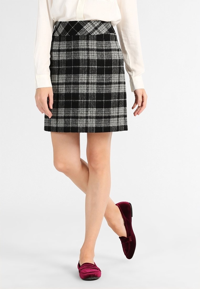 Jupe écossaise grise et noire avec une taille ajustée, tissu texturé et design évasé, associée à des ballerines bordeaux.